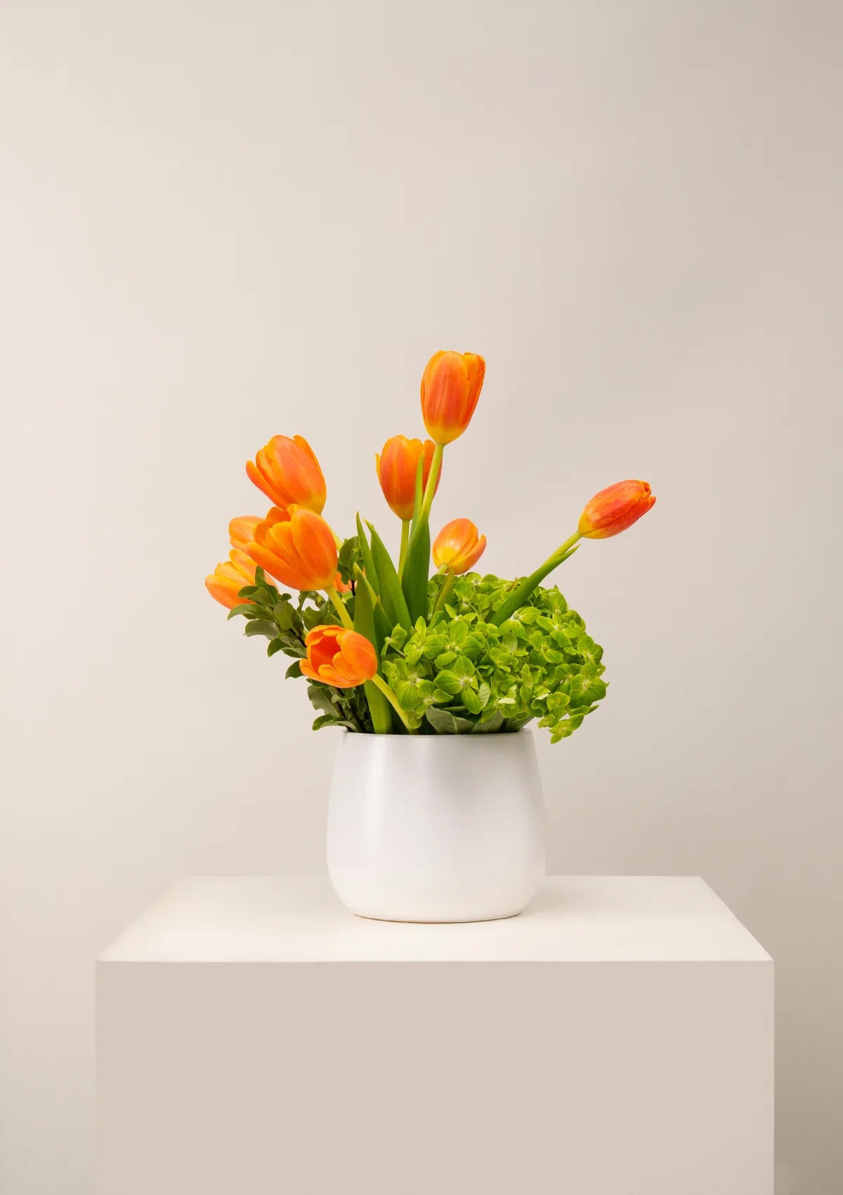 White Ceramic Lolanda Vase by Blooming Roots with Orange tulip flowers, Hydrangea Matcha, and greenery.