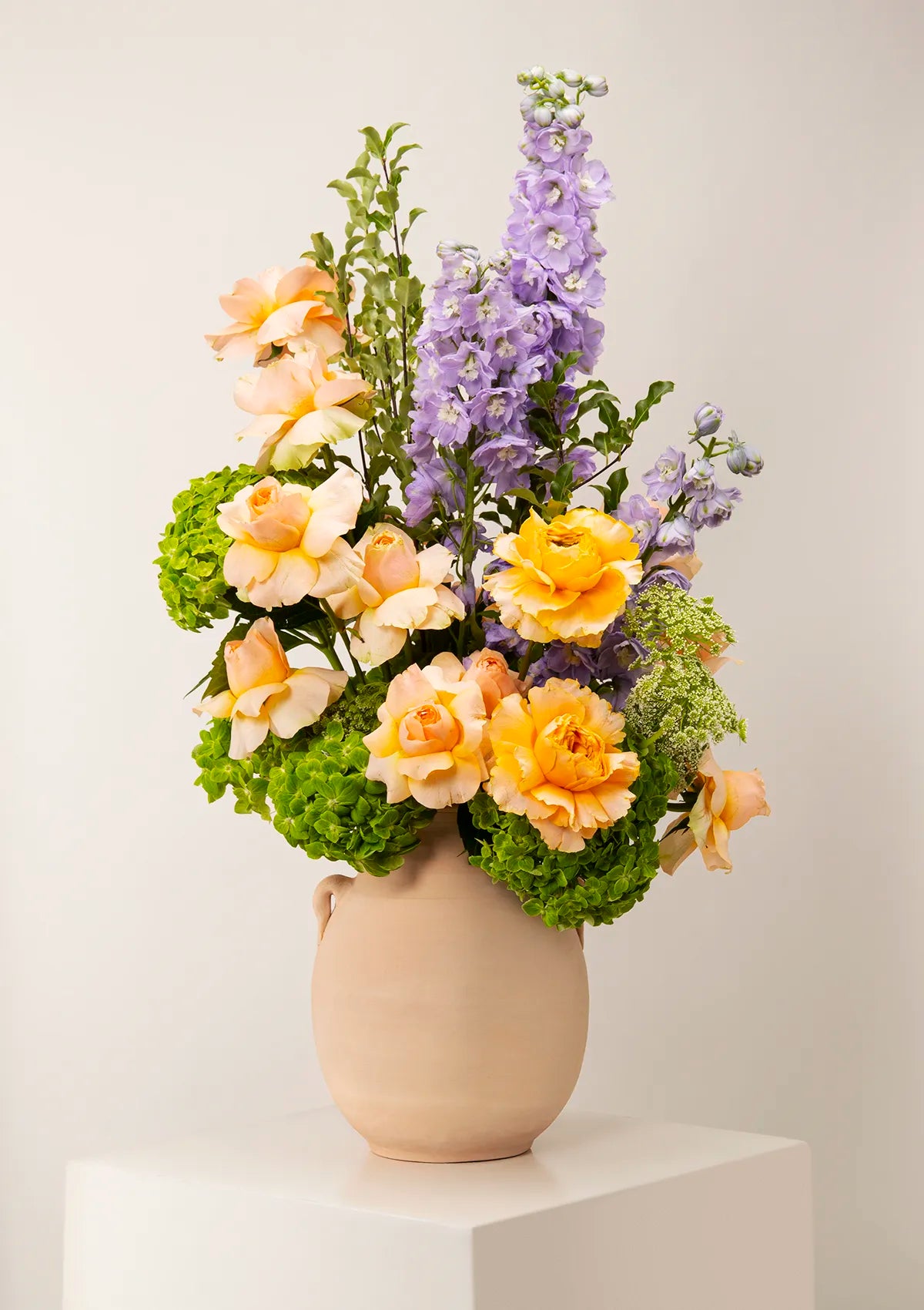 Light Beige Clay Magestic Bloom Vase by Blooming Roots with Orange roses, Hydrangea Matcha, purple flowers, and greenery.