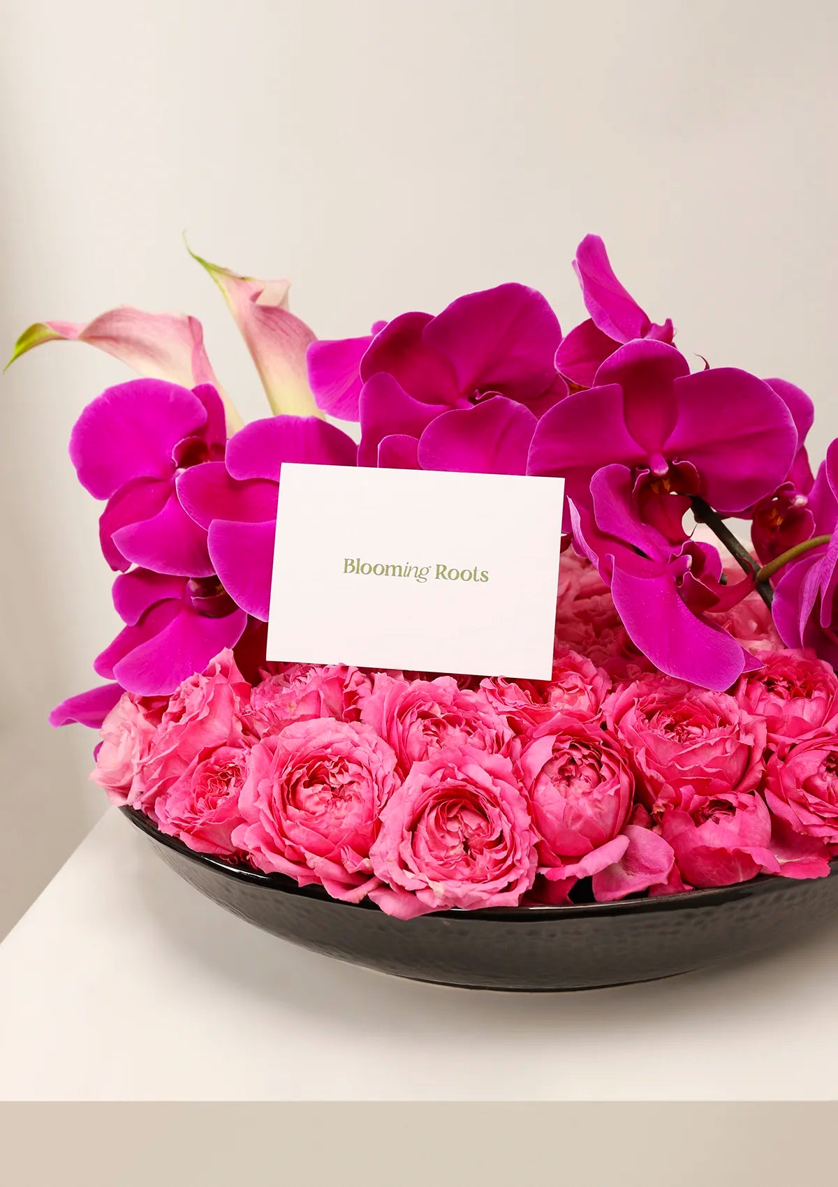 Sleeping Beauty black plate Arrangement by Blooming Roots with Phalaenopsis Cut Flowers Big Chilli, Spray Rose Julietta Cerise, Calla, and Eustoma Pink flowers